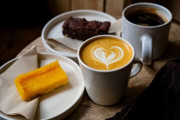 Coffee break. Two mugs of American and latte art on a wooden background. Chocolate brownie and yuzu cake slices. Delicious sweet food and coffees. Flat white, latte. Food and drink.