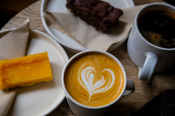 Coffee break. Two mugs of American and latte art on a wooden background. Chocolate brownie and yuzu cake slices. Delicious sweet food and coffees. Flat white, latte. Food and drink.