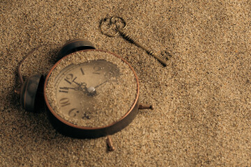 Vintage alarm clock and key on sand, closeup. Time management concept.