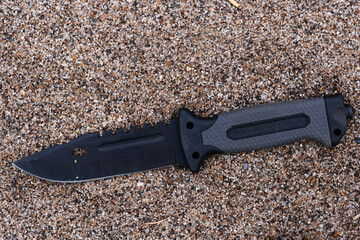 Obraz premium Knife with black handle on the sand of a beach. Top view.