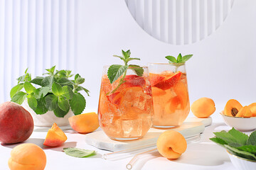 Ice peach tea or cocktail with mint and apricots, a recipe for a refreshing summer drink. Two glasses with peach fruit lemonade on a light table, detox diet and weight loss concept, 