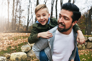 Obraz premium Nature, piggyback and dad with child in outdoor park for game, fun and bonding together. Forest, playing and happy man with boy on back for support, weekend trip or autumn weather in Washington