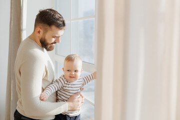 Serene portrait of father baby interaction by window, with dad attentive gaze and little son...