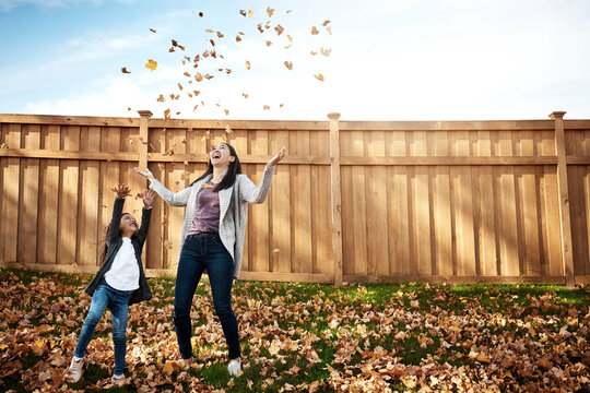 Autumn, mama and daughter throwing leaves in garden of home together for bonding or love. Asian family, excitement or fall with single parent woman and girl child having fun in backyard for wellness