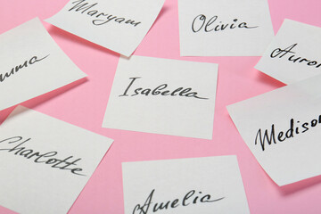 Paper stickers with different names on pink background, closeup. Choosing baby's name