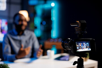 Focus on professional video production tech used for capturing footage on content creator filming various sketches for his internet channel. Vlogging camera and media star in blurry background talking