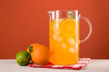 Freshly made lemonade in jug and citrus fruits on light wooden table