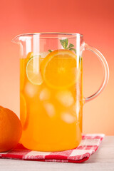 Freshly made lemonade in jug and orange on light wooden table