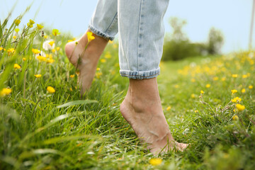 Woman walking barefoot on green grass outdoors, closeup
