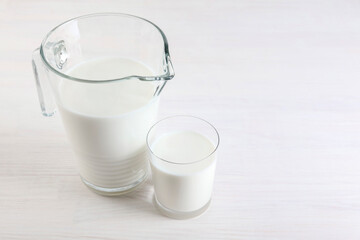 Jug and glass of fresh milk on wooden table, space for text