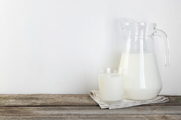 Jug and glass of fresh milk on wooden table, space for text