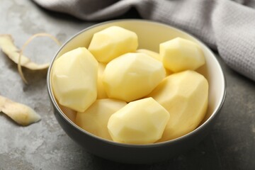 Fresh raw potatoes in bowl and peels on grey table, closeup