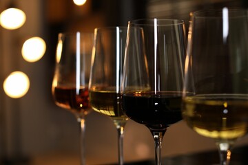 Different tasty wines in glasses against blurred lights, closeup