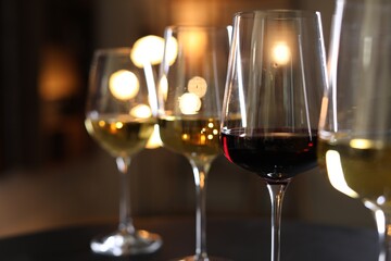 Different tasty wines in glasses on table against blurred lights, closeup