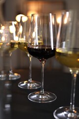 Different tasty wines in glasses on black table against blurred lights, closeup