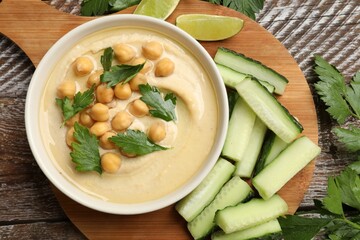 Tasty hummus with chickpeas in bowl and fresh products on wooden table, flat lay