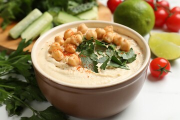 Tasty hummus with chickpeas in bowl and fresh products on light table, closeup