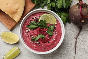 Tasty beet hummus with sesame in bowl served on grey textured table, flat lay