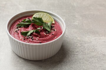 Tasty beet hummus with sesame and lime in bowl on grey textured table, closeup. Space for text