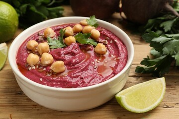 Tasty beet hummus with chickpeas and parsley in bowl on wooden table, closeup