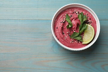 Tasty beet hummus with parsley and lime in bowl on light blue wooden table, top view. Space for text