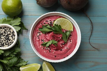 Tasty beet hummus in bowl and fresh ingredients on light blue wooden table, flat lay