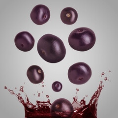 Acai berries falling into juice on grey background