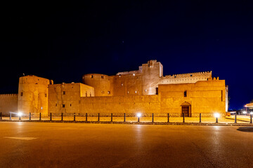 Jabreen citadel fortress stone walls and round bastion tower in night illumination, Bahla, sultanate Oman