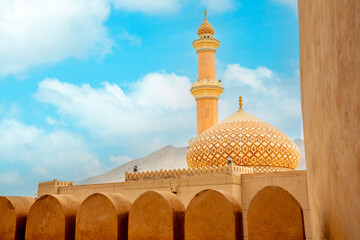 Al Qala'a Mosque ornated dome and minaret with Nizwa castle walls in the foreground, Nizwa,...