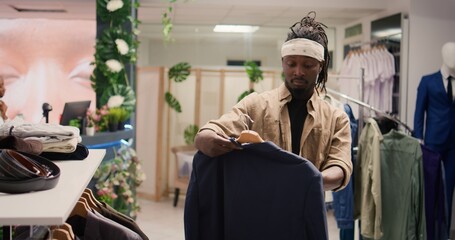 Shopper looking at elegant blazers and shirts in clothing store. Client analyzing garments on...