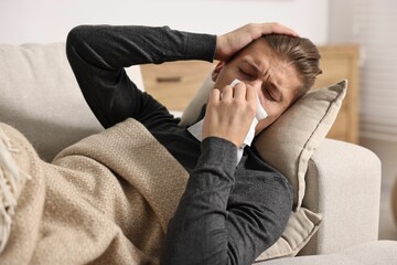 Young man with tissue suffering from sinusitis and lying in bed at home