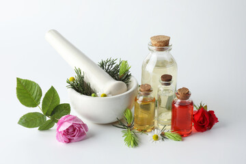 Aromatherapy. Different essential oils, flowers, mortar, pestle and fir twigs on white background