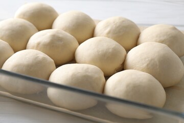 Raw dough balls in baking dish on white wooden table, closeup