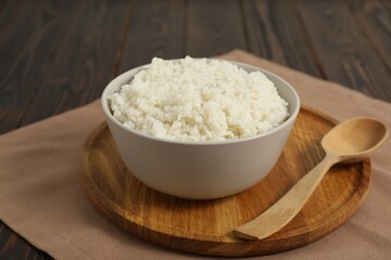 Delicious boiled rice in bowl and spoon on wooden table