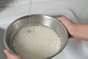 Woman rinsing rice in bowl above sink, closeup