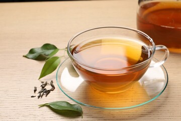 Refreshing green tea in cup and leaves on wooden table, closeup