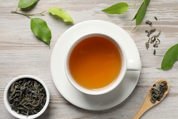 Refreshing green tea in cup, spoon and leaves on light wooden table, flat lay