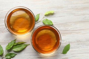Refreshing green tea in cups and leaves on light wooden table, flat lay