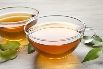 Refreshing green tea in cups and leaves on light wooden table, closeup