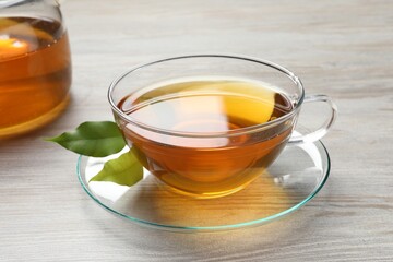 Refreshing green tea in cup and leaves on light wooden table, closeup