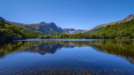 Fototapeta premium Peaceful lake surrounded by lush green hills and mountains under a clear blue sky 