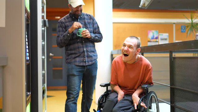 Man with cerebral palsy laughing next to coworker during a work break walking into vending machines