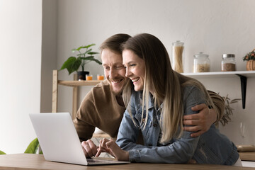 Married couple searching for dream house on internet, looking through real-estate agencies using laptop, make purchase online, buy goods, enjoy leisure online, watch videos in social media, websurfing