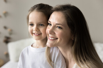 Close up portrait of pretty young mother and little daughter, smiling looking away in morning at home. Family bond and ties, happy woman enjoy motherhood, spend time with adorable preschooler child