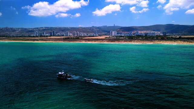 Aerial Backward Panning Shot Of Nautical Vessels Moving On Wavy Sea In City Under Cloudy Sky - Haifa, Israel