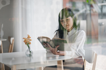 A young woman enjoys reading a book while sitting at a modern cafe with minimalist decor and natural light streaming through the window.