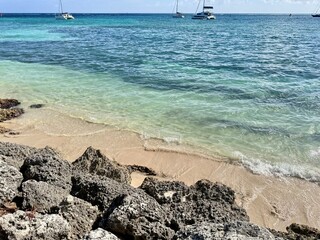 close-up of a small wild sandy beach with rocks and a turquoise sea with boats in Guadeloupe in the...