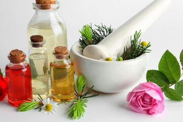 Aromatherapy. Different essential oils, flowers, mortar, pestle and fir twigs on white background