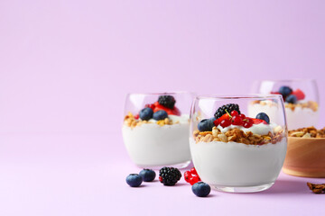 Tasty yogurt with fresh berries and granola in glasses on violet background, space for text