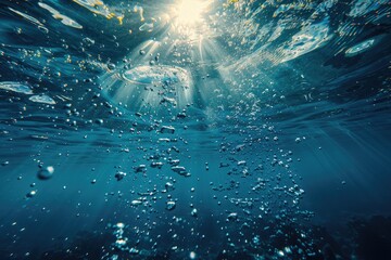 A clear blue ocean with sunlight shining through the water. The water is full of bubbles and the sunlight is reflecting off of them